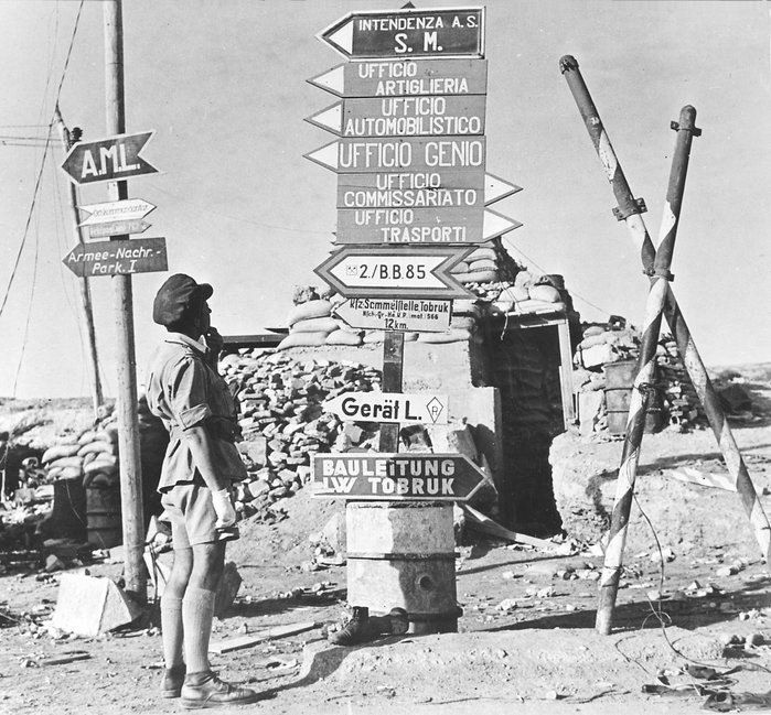 1942년, 연합군 병사 한 명이 독일어와 이탈리아어로 쓰여있는 토브룩의 도로 안내표지를 보고 있다. < 출처: Public Domain>